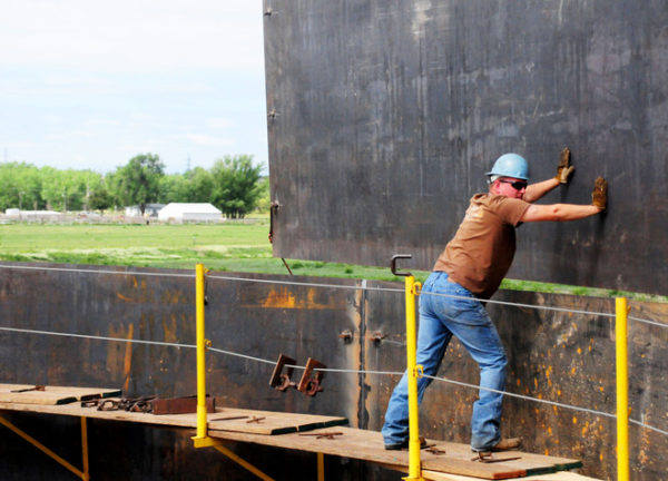 Pushing on a sheet of metal during construction of an aboveground liquid storage tank.